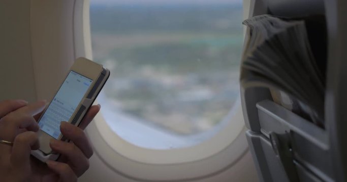 Woman texting on smart phone by the illuminator in flying airplane