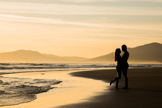 Lovers at sunset holding looking at each other on a beach silhouettes