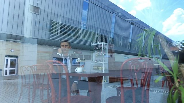 Business man receiving a call while drinking coffee in bright cafe, ald waks out