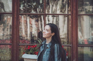 Fototapeta premium Summer lifestyle portrait of hipster woman walking in city, smiling enjoy weekends, travel with backpack. Female in casual jeans clothes near building, flowers in Europe.