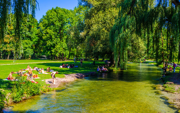 People are sunbathing and having a picnic next to an artificial creeking inside of the english garden in bavarian city munich