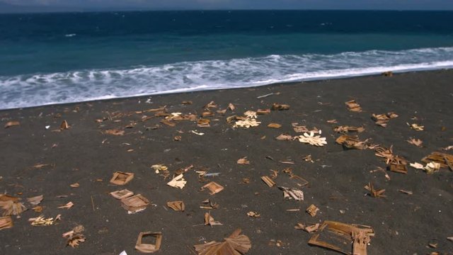 Scattered cardboard and other forms of litter, strewn along a stretch of tropical, volcanic, black sand beach in Bali, Indonesia. Video 4k