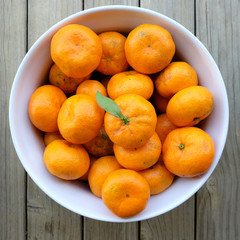 Imperfect blemished organic satsuma mandarins. Citrus fruit is in a white bowl, photographed from above with a wooden background.