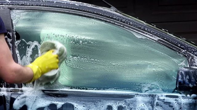 closeup of professional car washer cleaning car window with soapy sponge.