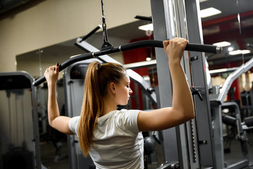 Fototapeta premium A young sportswoman working our seriously in a big gym. Training for strength of the back muscles