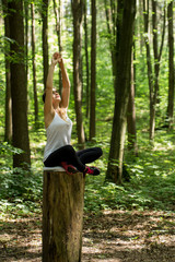 Beautiful sporty girl in the woods on a stump in yoga, sports