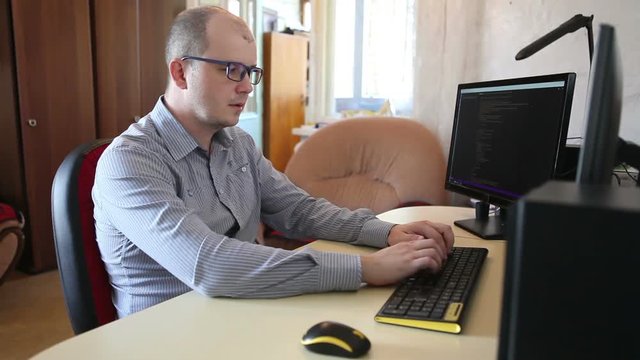 male programmer fixes the code sitting at the computer. side view