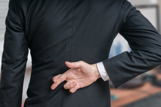 Businessman has crossed fingers behind his back. Good luck or dishonesty concept.