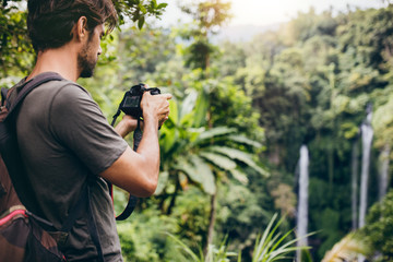 Man with backpack taking a photo of waterfall
