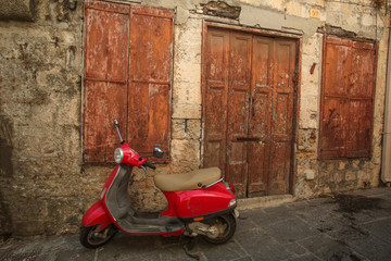 Fototapeta na wymiar Red scooter near the old stone wall with wooden door and wondow