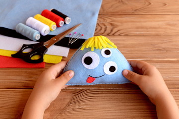 Child holds a felt monster in his hands. Funny soft toy for kids. Sewing craft supplies and tools on a wooden table. Felt Halloween ornament. Easy sewing fabric monster doll