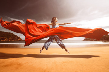 Obraz na płótnie Canvas Frau springt am Strand zwischen fließenden Stoffen