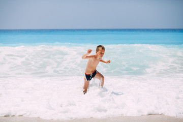 Beach vacation dream. Handsome young boy enjoying in beautiful tropical beach, running and playing with waves.