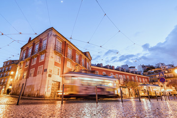 City lights on the typical architecture and old streets at dusk while the tram 28 proceeds, Alfama, Lisbon, Portugal