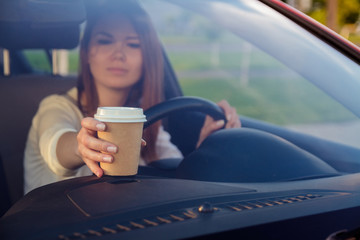 Young, beautiful woman with coffee in hand behind the wheel of a car. Don't sleep and drive