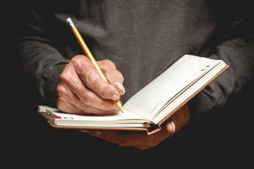 An elderly man wrote in pencil in a notebook. Photo in low key - obrazy, fototapety, plakaty