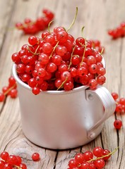 Fresh organic red currants in a cup on the old wooden table.