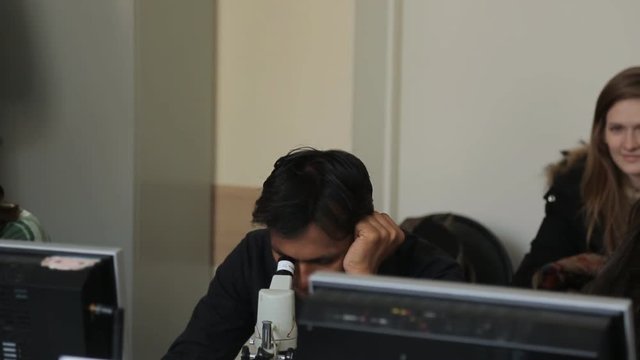 Indian man looks through a microscope in classroom for biology.