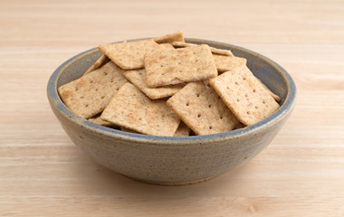 Bowl of organic whole wheat crackers on a wood table side view.