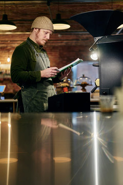 Male coffee shop owner at coffee roaster with clipboard