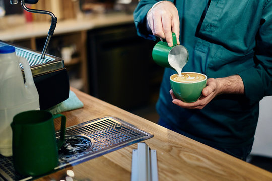 Cropped shot of male barista pouring milk into coffee cup in coffee shop