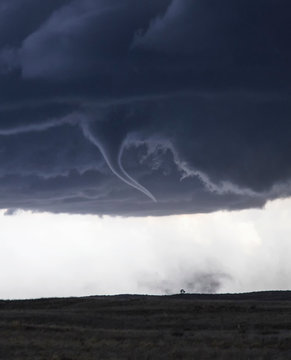Tornado with funnel cloud over field landscape