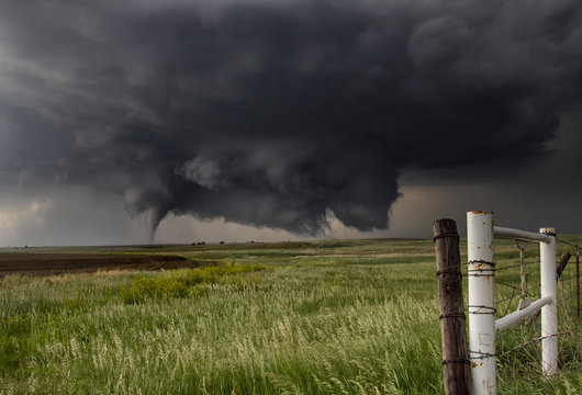 A large cone tornado touches down in an open country field from a very large angled ground-scraping wall cloud