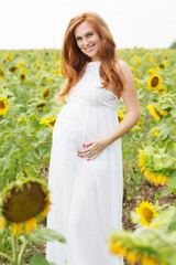 Naklejka na ściany i meble Pregnant girl in the field with sunflowers