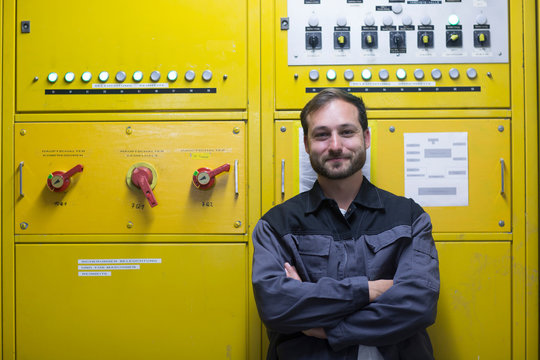 Man in front of yellow control panel, arms crossed smiling