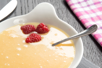 Crema pasticcera con lamponi rossi nel contenitore in ceramica su un tavolo