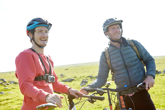 Cyclists on hillside holding bicycles looking away