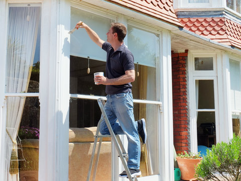 Man on ladder painting window frame