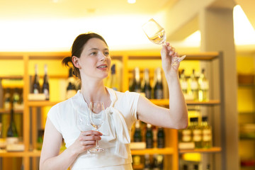Woman in wine shop holding up wine glass checking cleanliness