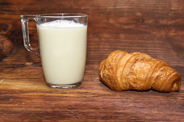 The morning breakfast of milk and croissant on a wooden table.