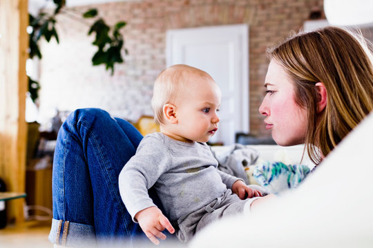 Mid Adult Woman And Baby Daughter Pulling Faces On Sofa