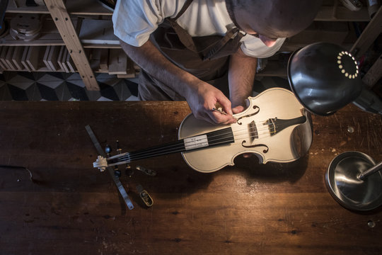 Luthier adjusting the sound post of an unvarnished violin in his workshop