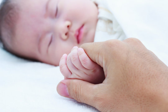 Close up hand of parent clasping hand of sleeping child.