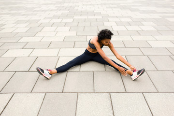 Woman sitting on pavement legs apart doing stretching exercises