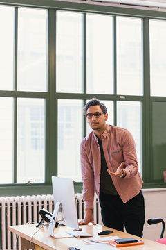 Man in office leaning against desk gesticulating
