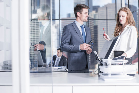 Businessman and businesswomen chatting by photocopier in office, colleagues using computer in background