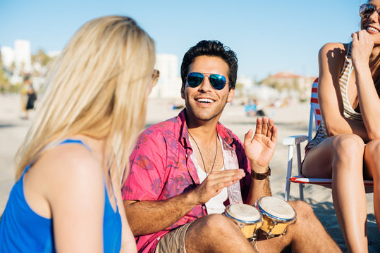 Young man with friends bongo drumming on beach, Santa Monica, California, USA