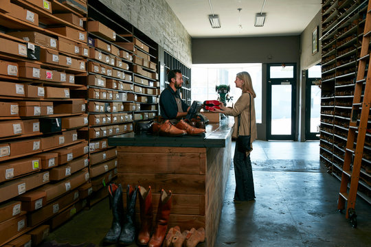 Cobbler serving female customer in traditional shoe shop