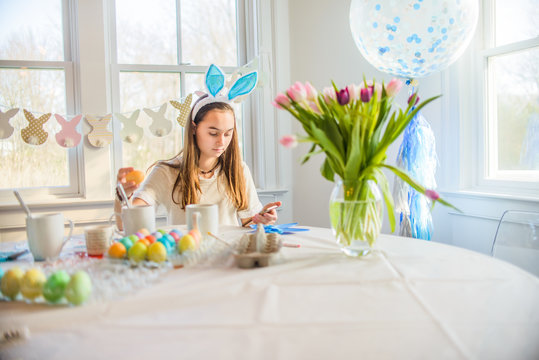 Teenage girl reading texts whilst dyeing hard boiled eggs for Easter at table