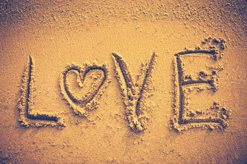 Text LOVE handwritten on seashore sand. Vignette and vintage tone