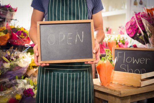 Male florist holding open sign on slate at his flower shop
