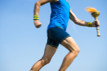 Torchbearer athlete in blue running with sport torch in motion blur across sunny blue sky