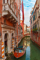 Obraz na płótnie Canvas Colorful narrow lateral canal and pedestrian bridge in Venice with docked boats, Italy