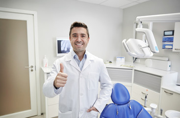 Naklejka na ściany i meble happy male dentist showing thumbs up at clinic
