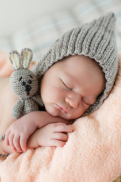 Cute girl in a gray knitted cap,put the handle under his head and hugging toy gray Bunny with big ears, sleeping on a pink blanket on a gray background
