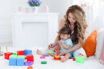 A young mother,blond with curly hair,was playing with his little daughter in a logical educational games,pyramid and collect the colored blocks,the daughter is a brunette with two tails on the head